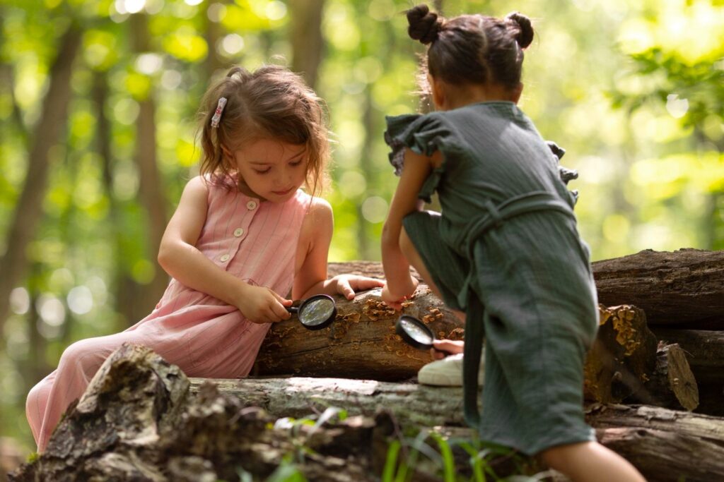 Girls with magnifying glass looking under a log